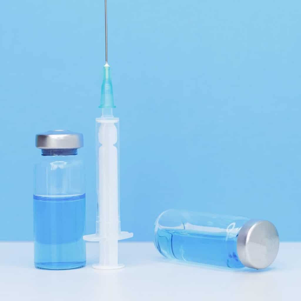 Close picture of a syringe and a flask on a laboratory table. Perform light-obscuration particle matter testing. Regulatory requirements for injectable parenteral products. Usp 788. Particle matter requeriments
